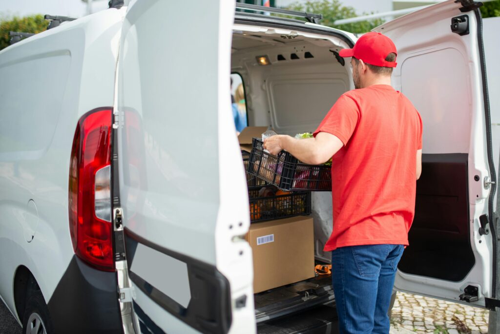 pexels photo 7843961 7843961 A courier in a red cap loads a delivery van with packages and a basket outdoors in Portugal.